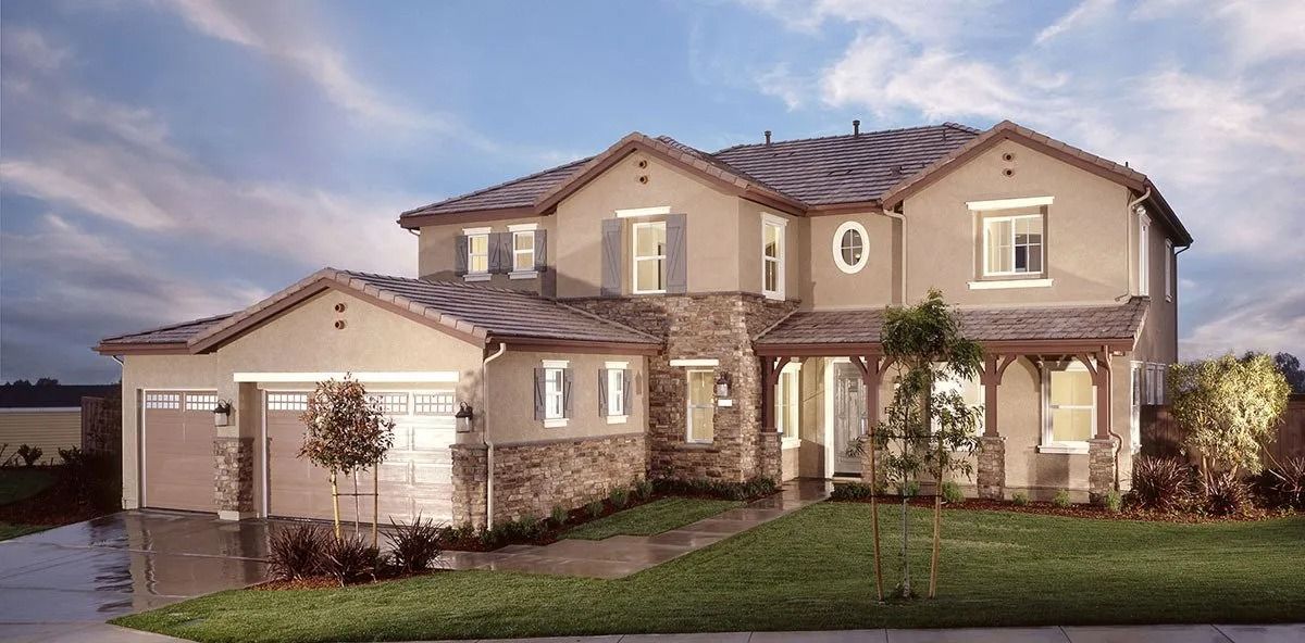 Beige two-story house with a stone facade, front porch, and garage, set on a green lawn against a cloudy sky.