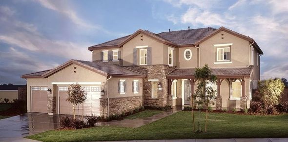 Beige two-story house with a stone facade, arched entrance, and a green lawn on a cloudy day.