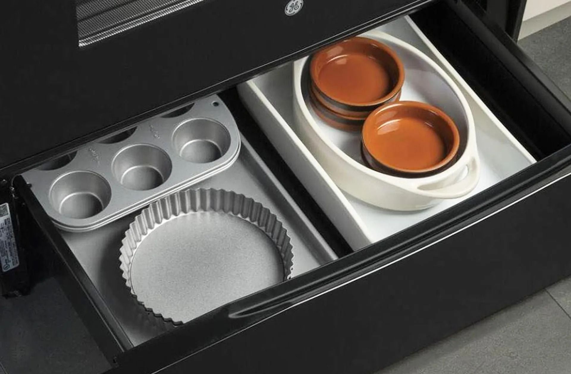 Open kitchen drawer with baking pans and ramekins.