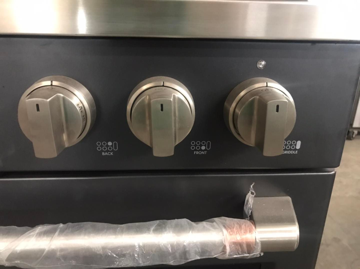 Close-up of a black oven control panel with three silver knobs and a silver handle.
