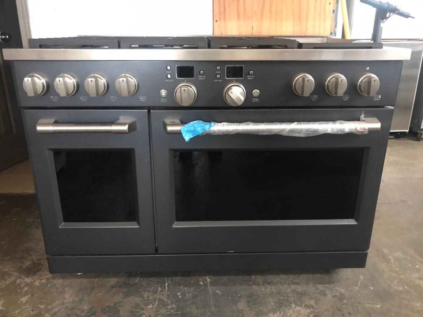 Dark gray gas range with stainless steel trim and knobs. Two oven doors and six burners visible.