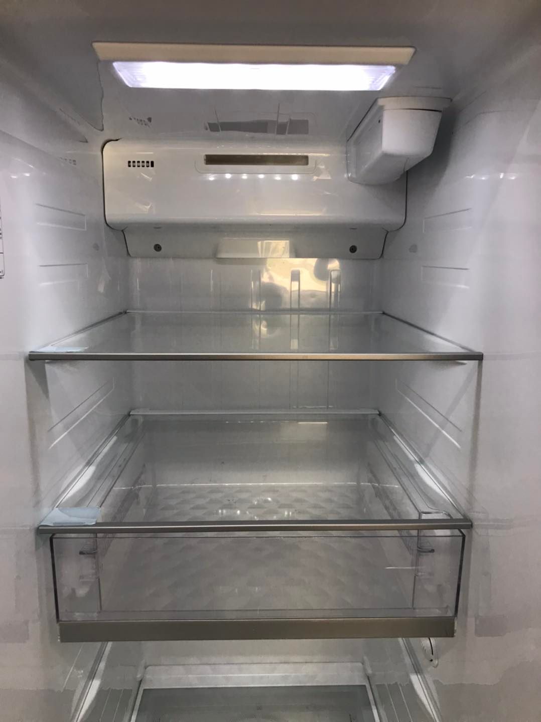 Empty white refrigerator interior with glass shelves and lighting.