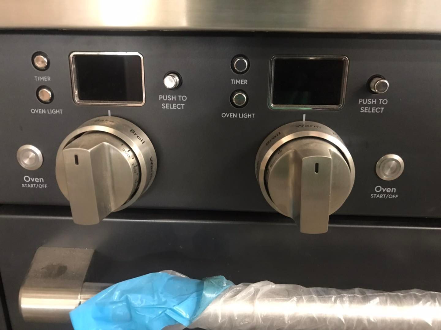 Close-up of a dark oven control panel with two digital displays, knobs, and buttons.
