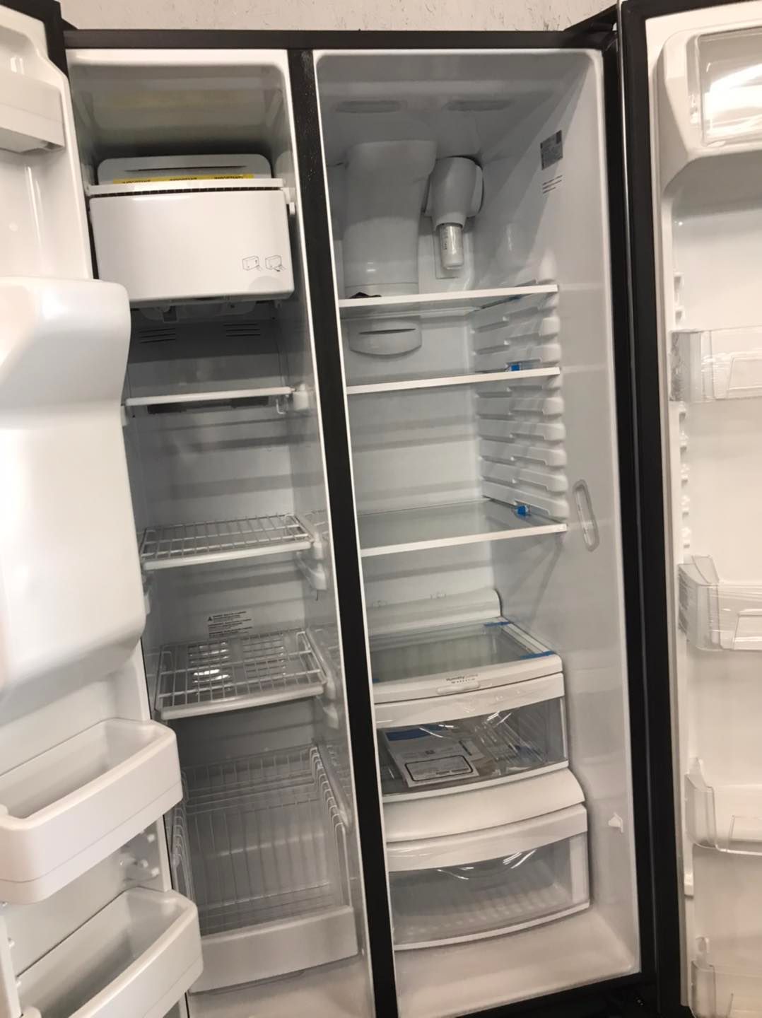 Open empty side-by-side refrigerator. Interior has shelves, bins, ice maker, and water dispenser.
