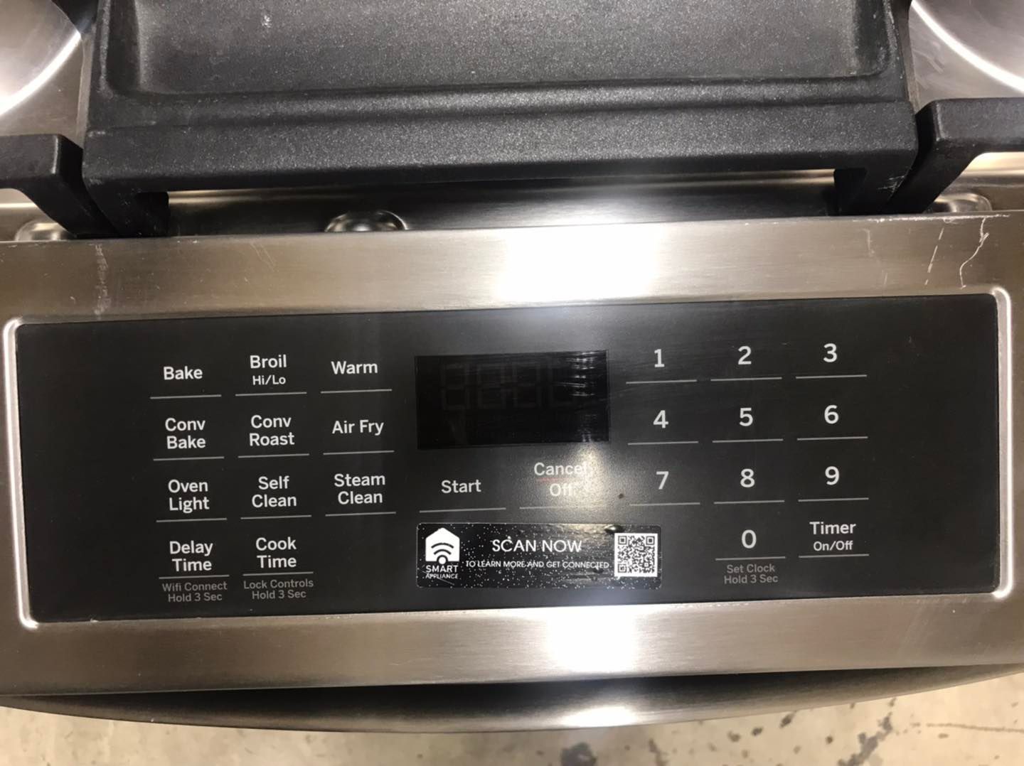 A stainless steel oven control panel with various buttons, a digital display, and a partially visible griddle above.