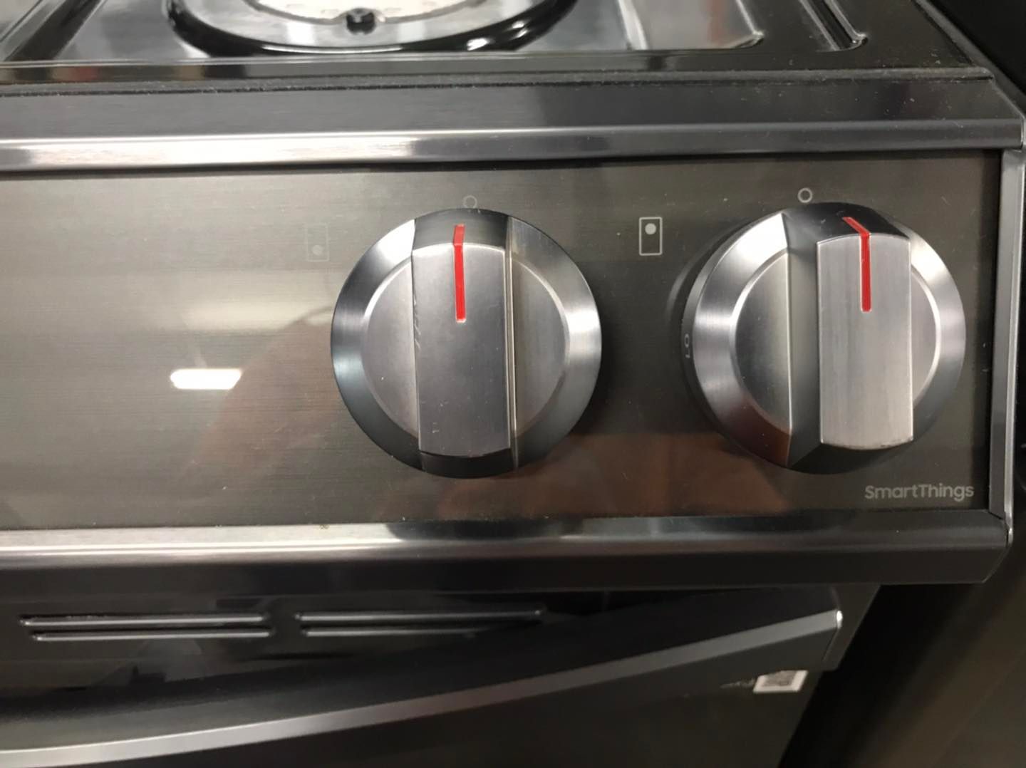 Close-up of a stainless steel oven control panel with two round knobs and red indicators.