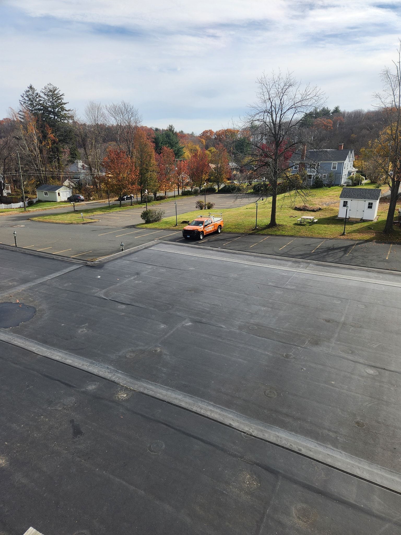 Asphalt parking lot with an orange vehicle and houses in the distance under a cloudy sky.