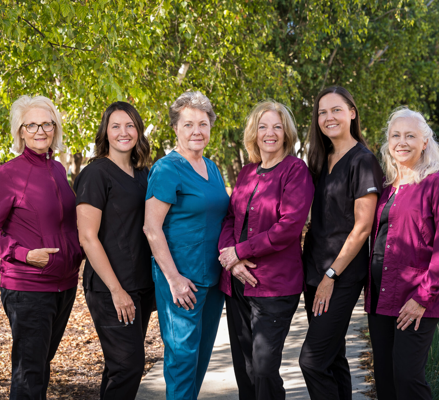 Six people in scrubs, standing outdoors; some wearing purple, black, or blue.