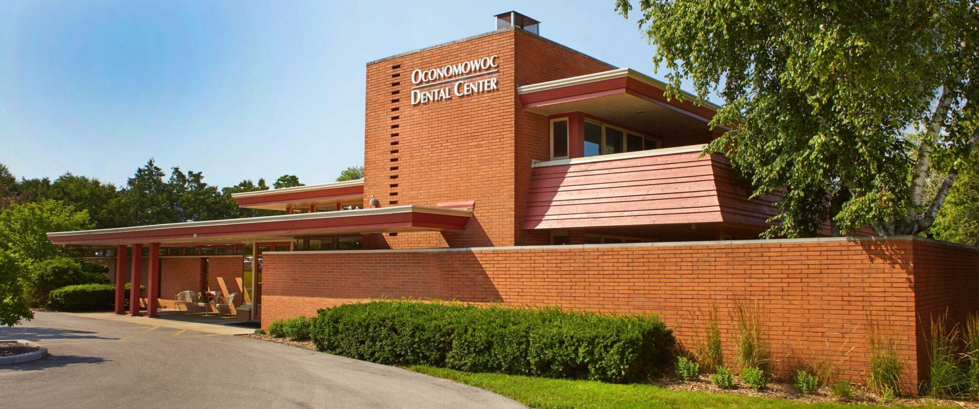 Red brick building with a flat roof, surrounded by green foliage, and a blue sky in the background.