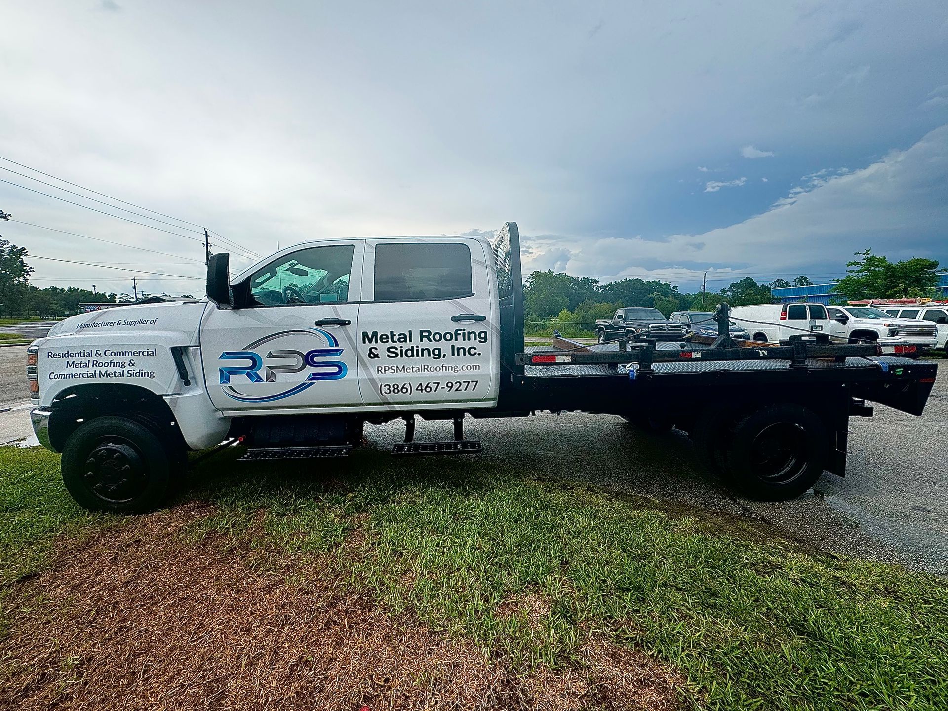 White flatbed truck with business logo parked on grass, cloudy sky in the background.