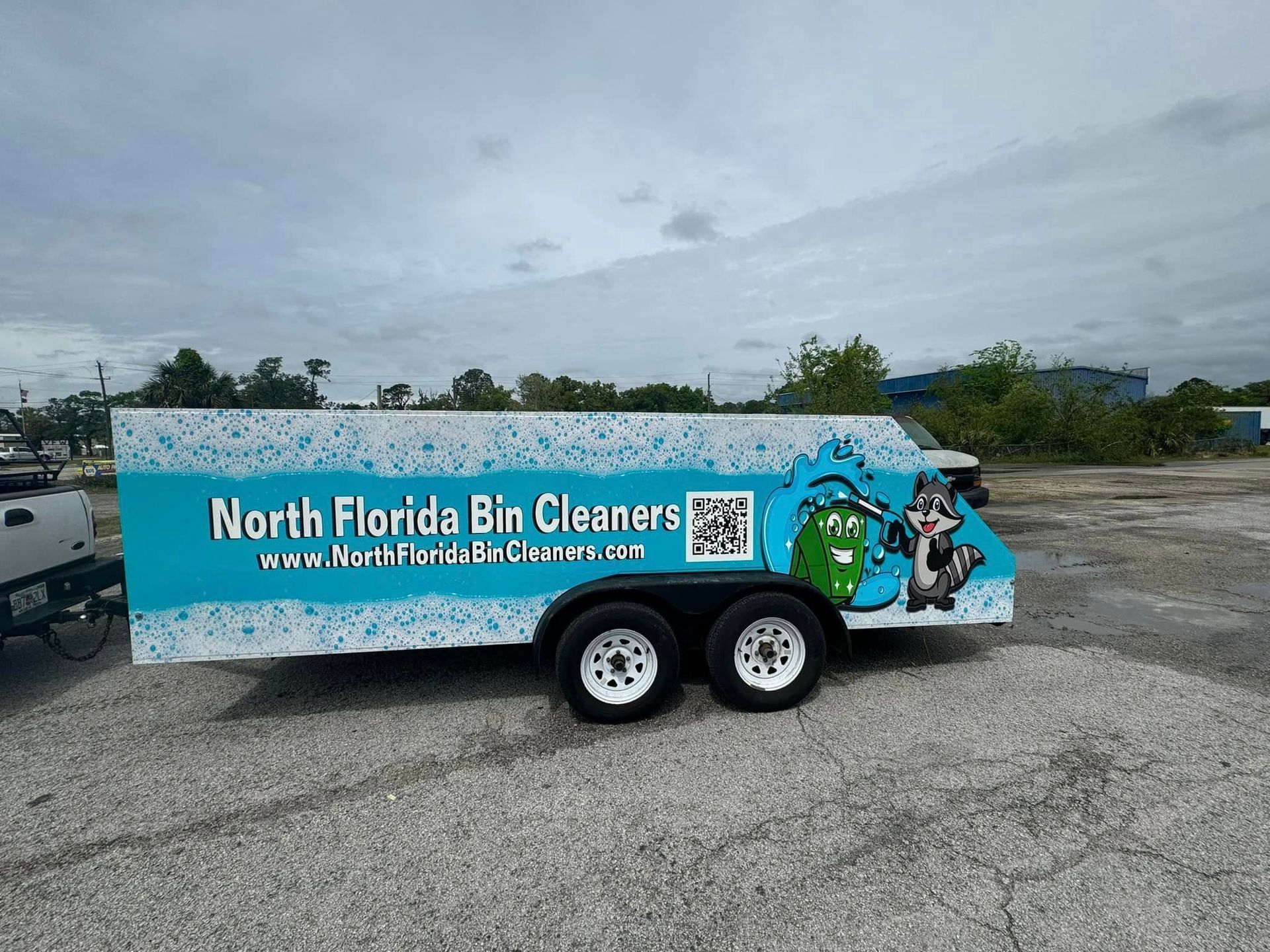 A trailer for North Florida Bin Cleaners, featuring a teal and white design, a raccoon mascot, and the company's logo.