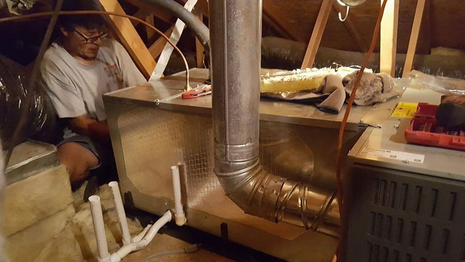A man is working on an air conditioner in an attic.