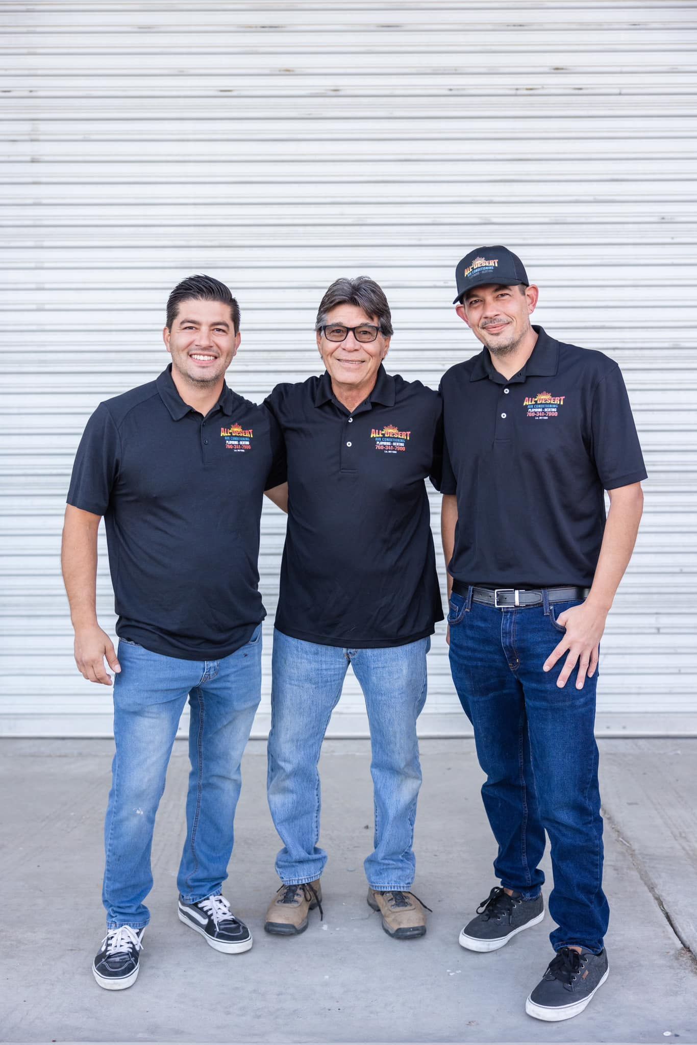 Three men are standing next to each other in front of a white garage door.