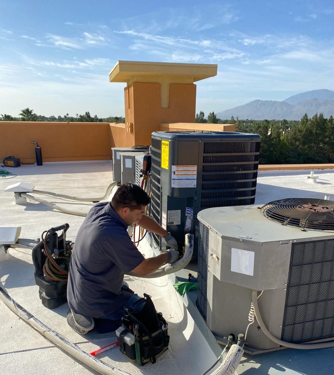 A man is working on an air conditioner on a roof