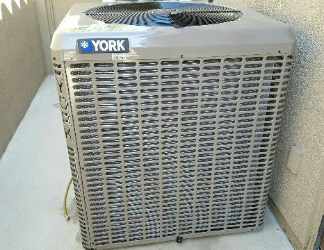 A york air conditioner is sitting on the sidewalk next to a wall.