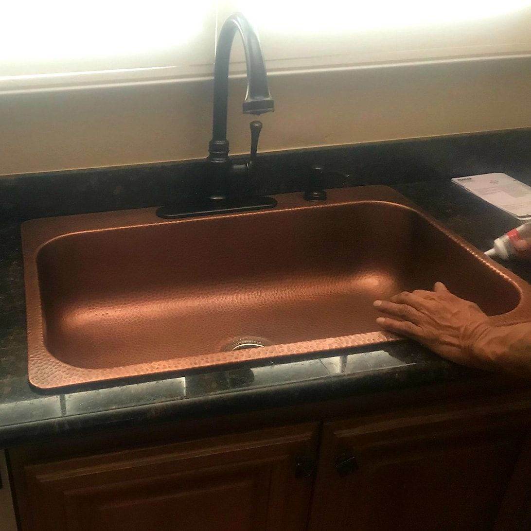 A person is cleaning a copper sink in a kitchen