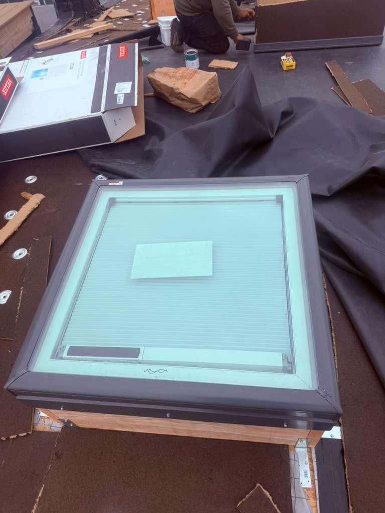 Skylight on a rooftop, surrounded by roofing materials. A person is visible in the background.