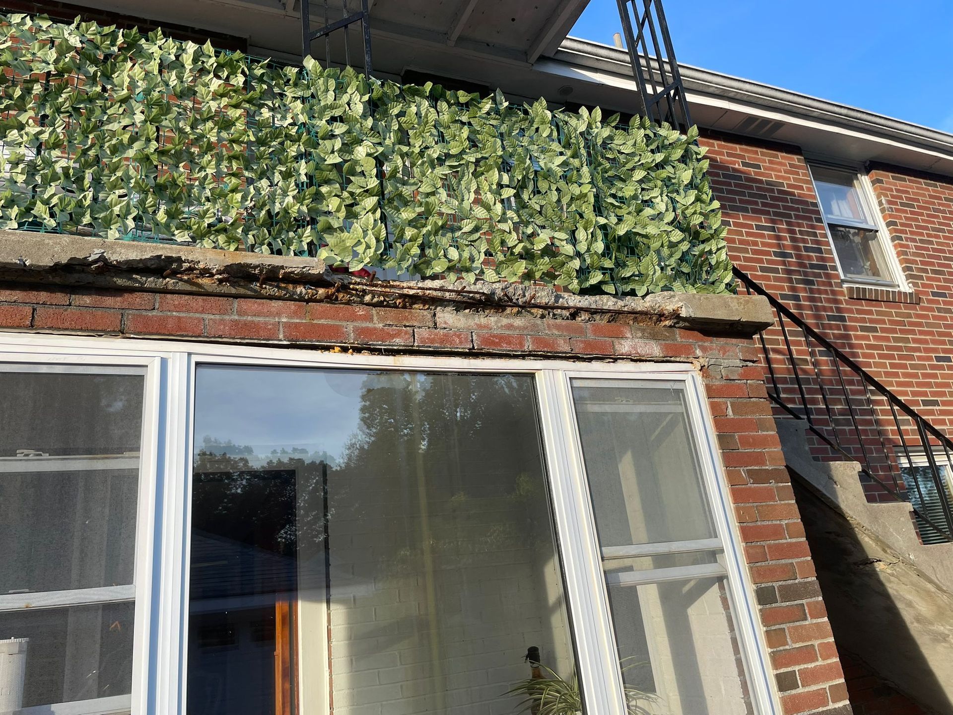 Brick building with balcony covered in artificial greenery, windows below.