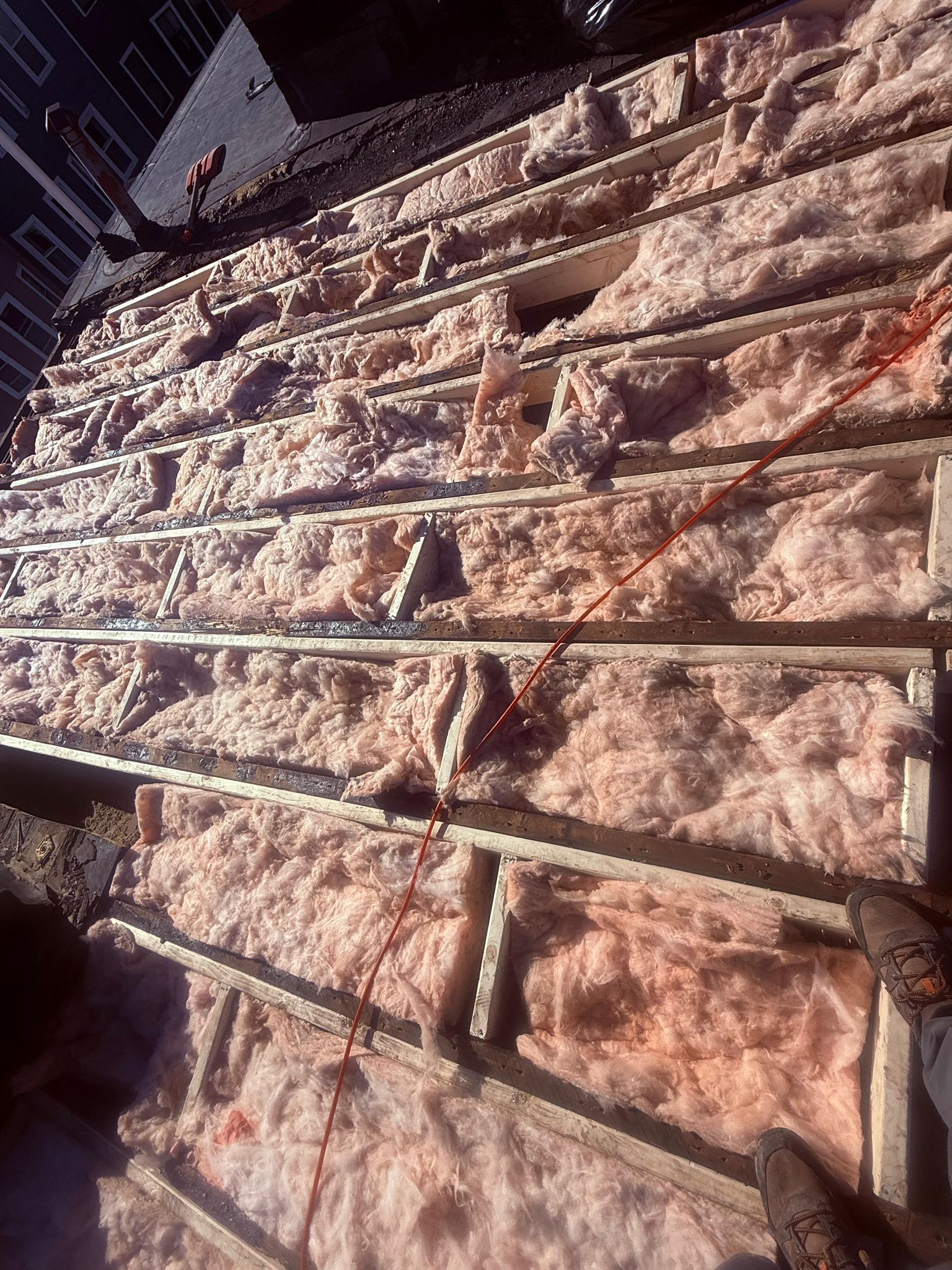 Pink insulation installed between wooden rafters on a roof.