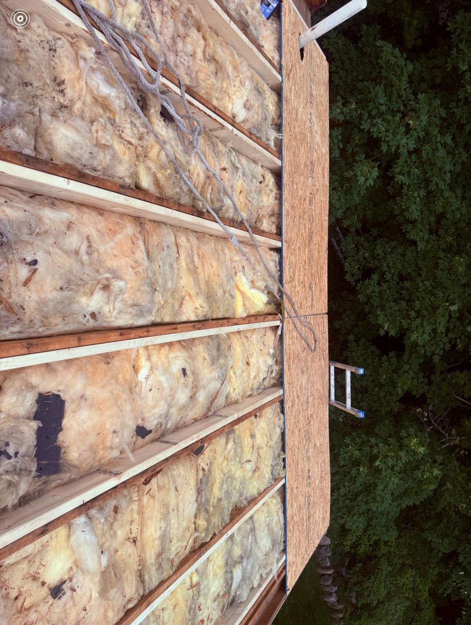 Overhead view of a roof under construction. Insulation and exposed wood beams are visible, with a section covered in plywood.