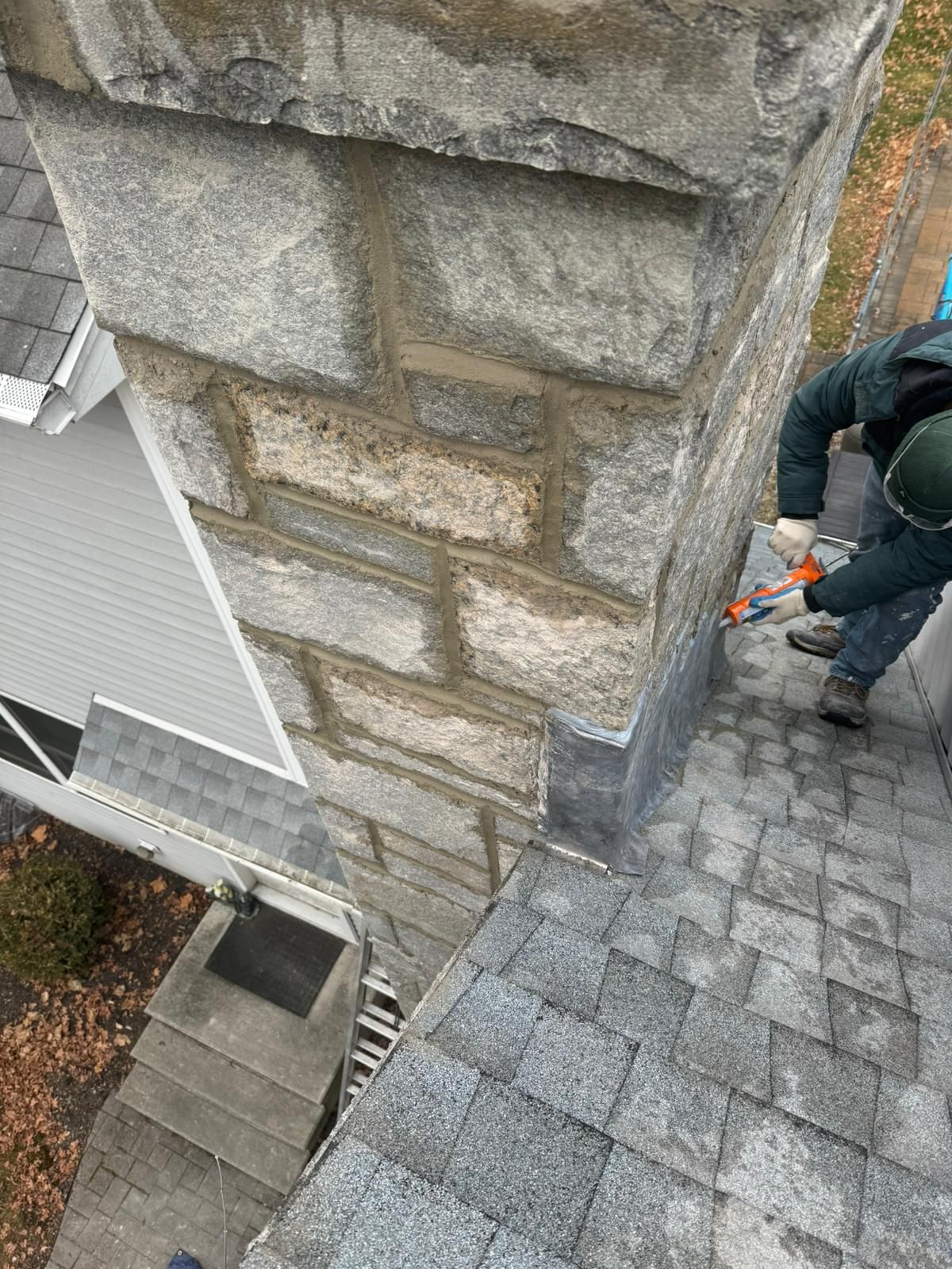 Person sealing a chimney with gray stone blocks on a rooftop.