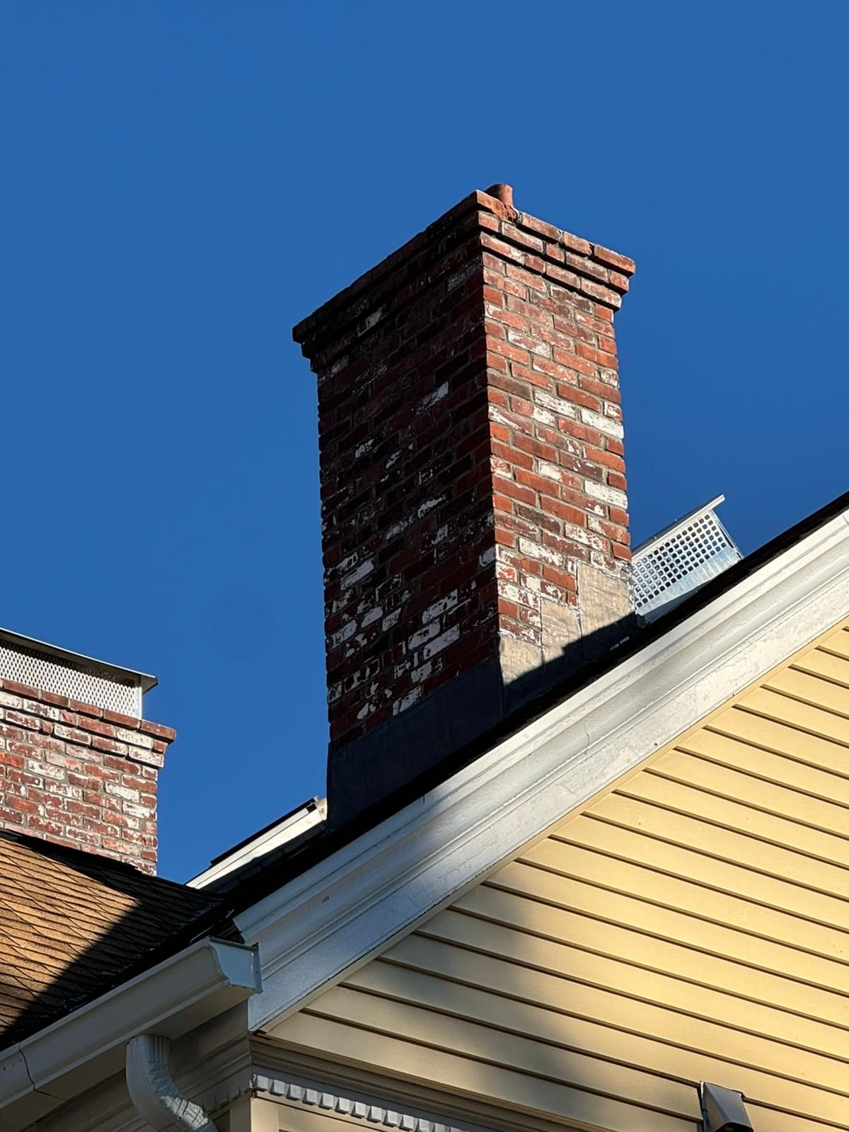 Brick chimney on a yellow-sided house against a clear blue sky.