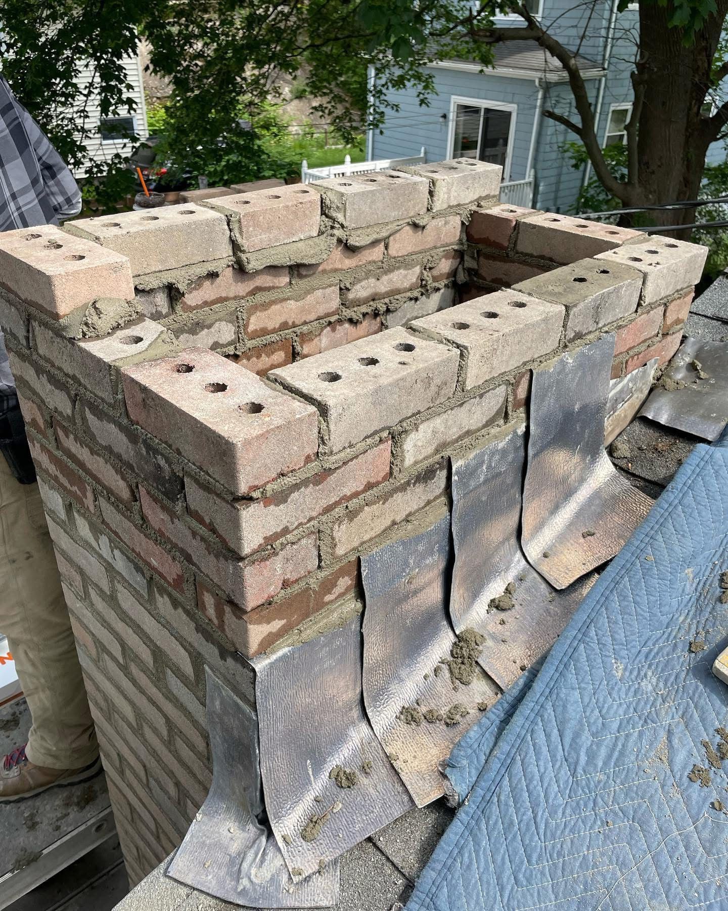 Chimney under construction with exposed brick, mortar, and roofing materials.