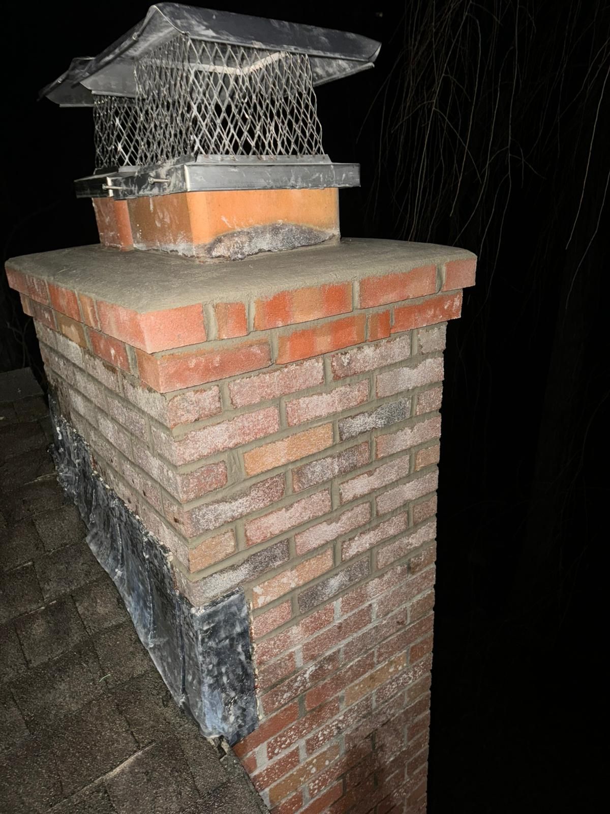 Brick chimney on a dark roof with a metal cap.