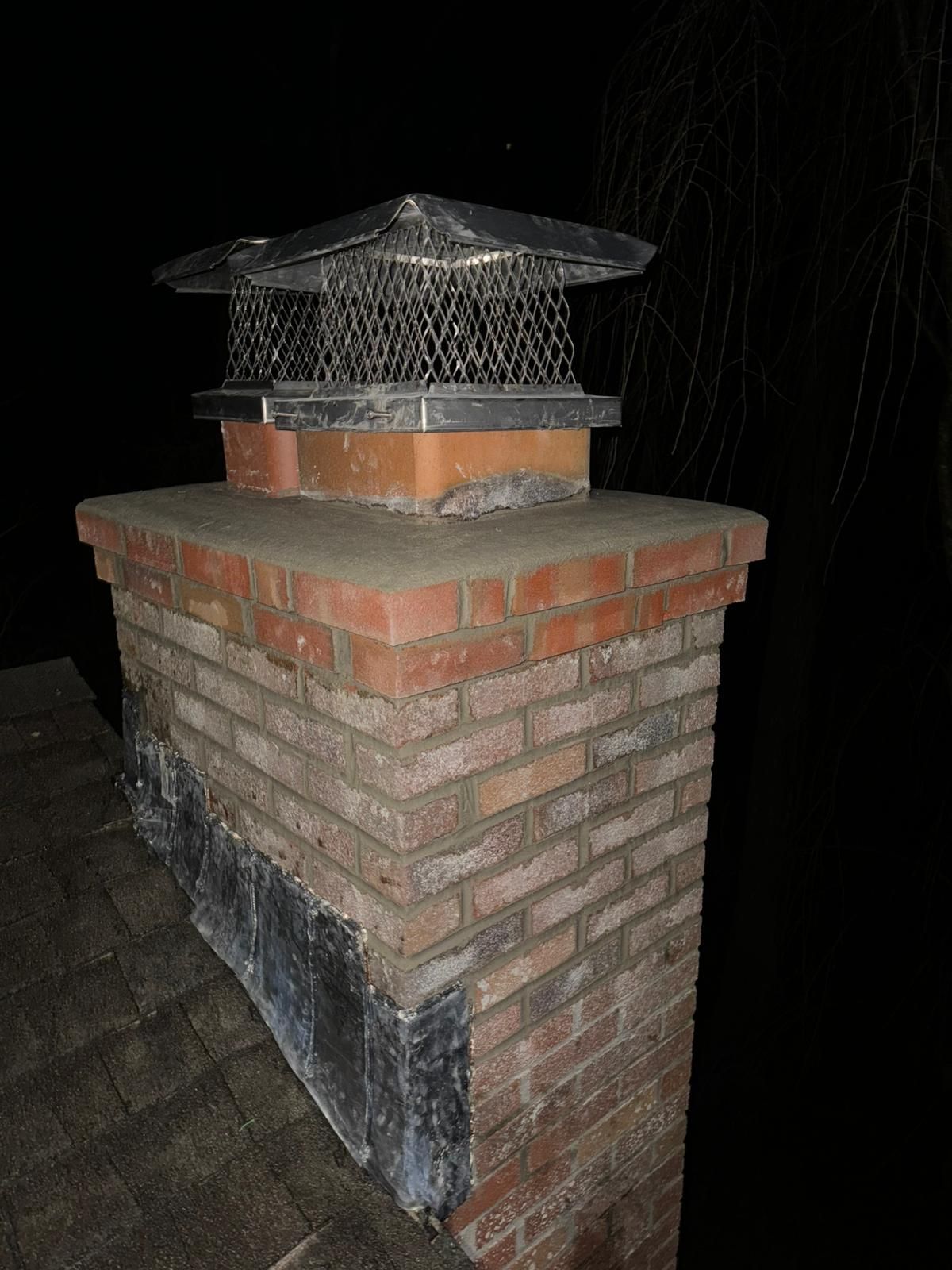 Brick chimney with metal cap, on a roof at night.