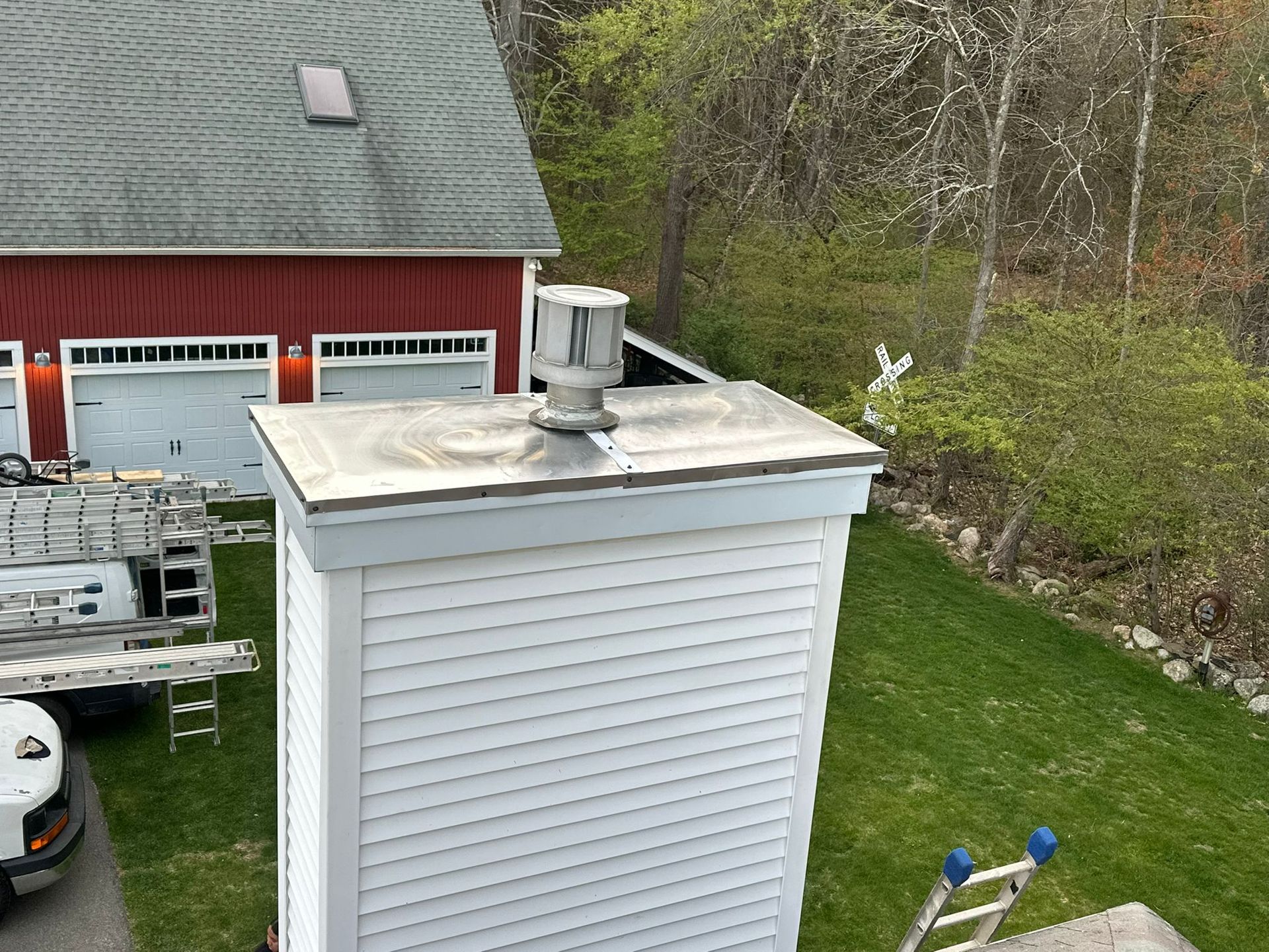 Chimney with a silver cap on a white-sided structure next to a red building and green lawn.