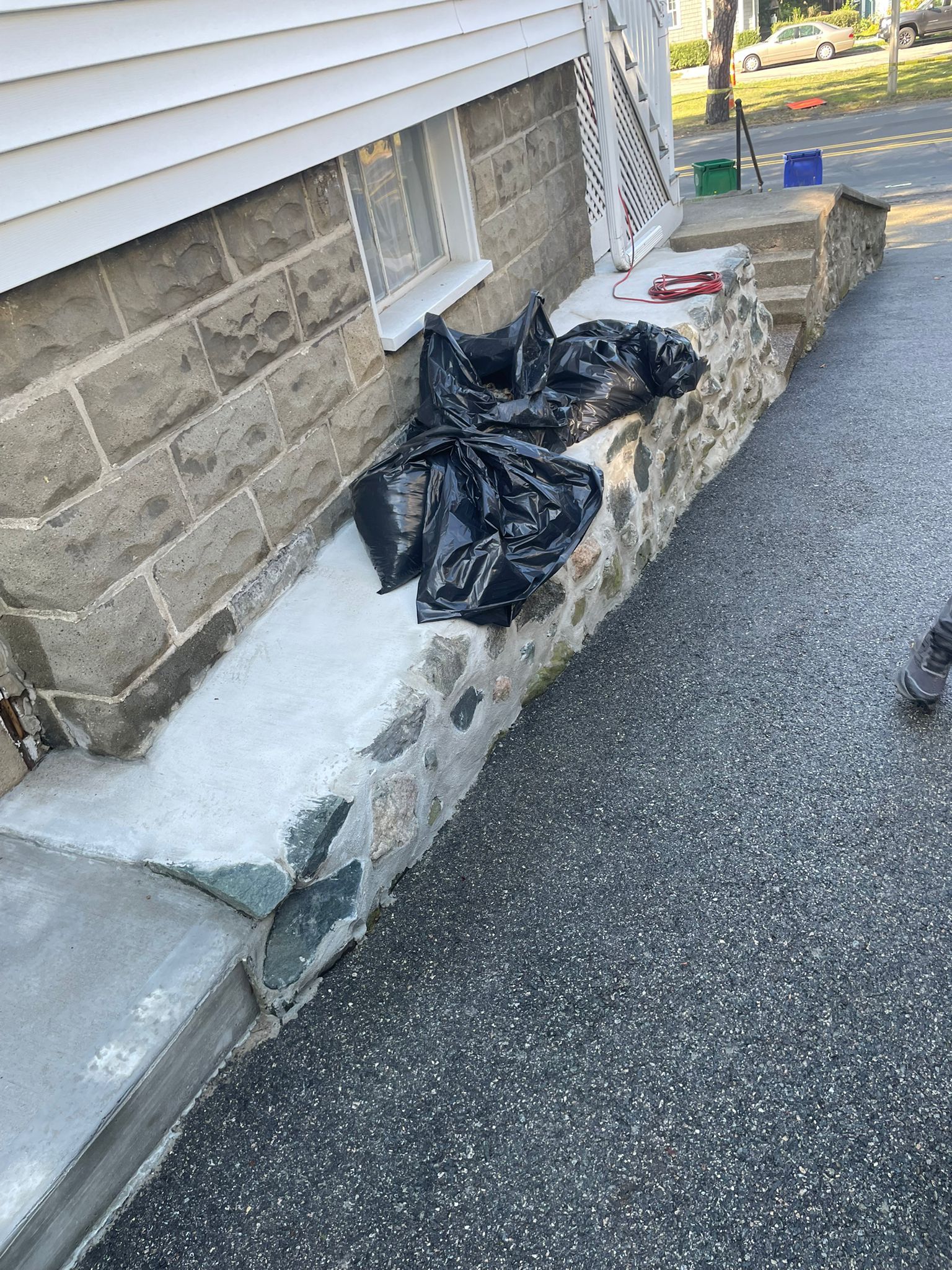 Stone wall with black trash bags on a concrete ledge next to a dark driveway.