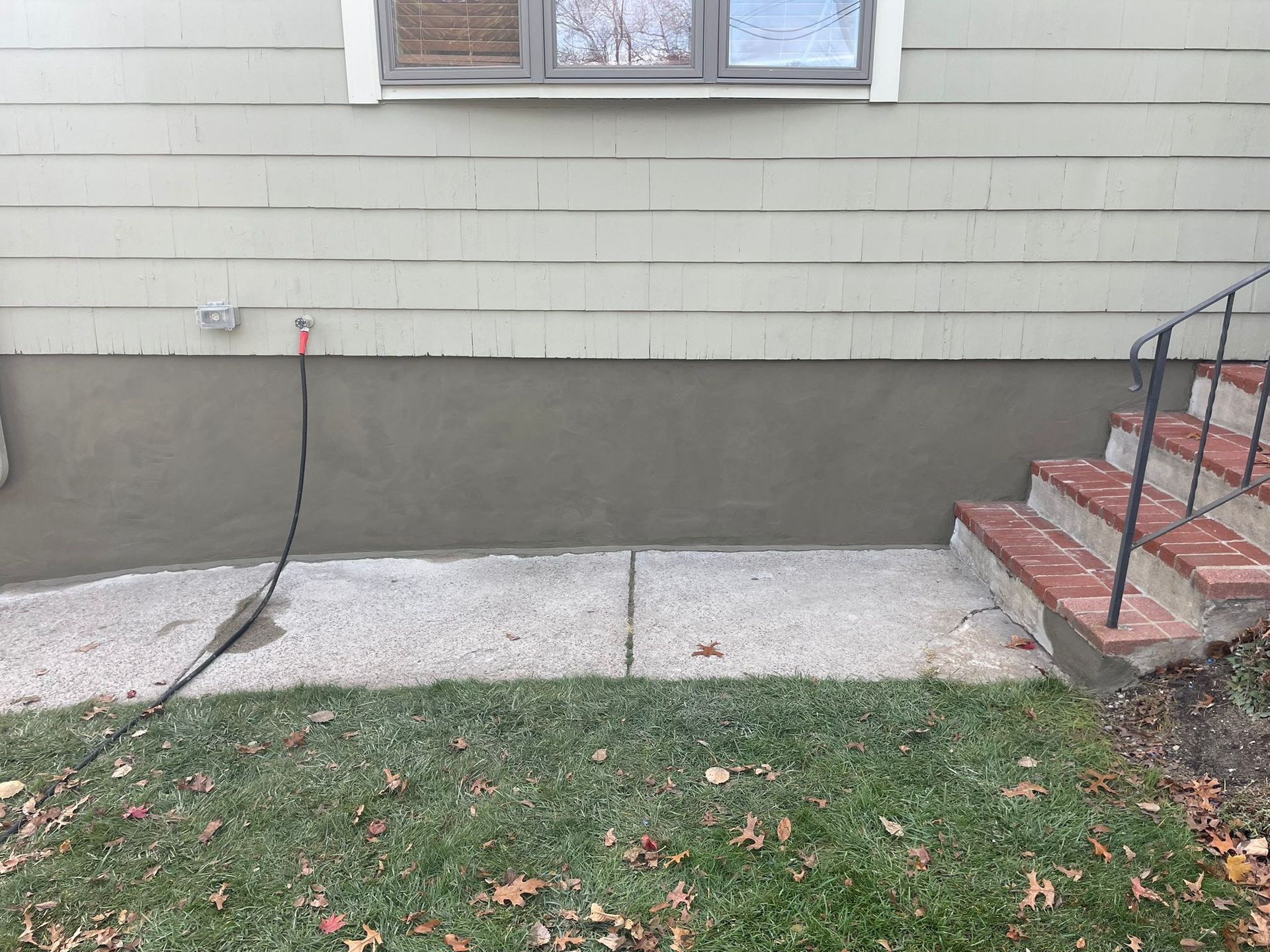Exterior wall with fresh gray stucco, concrete path, brick steps, and grass.