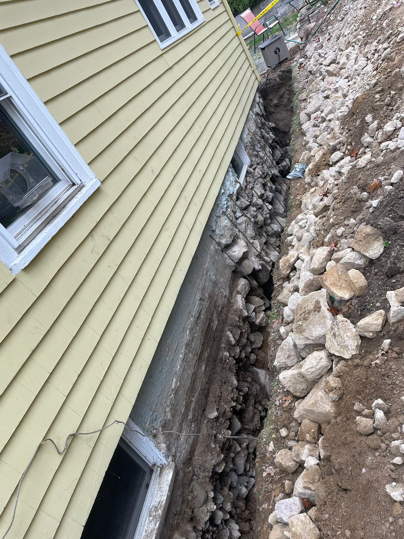 Trench dug beside a yellow house. Rocks and dirt are in the trench and on the ground.