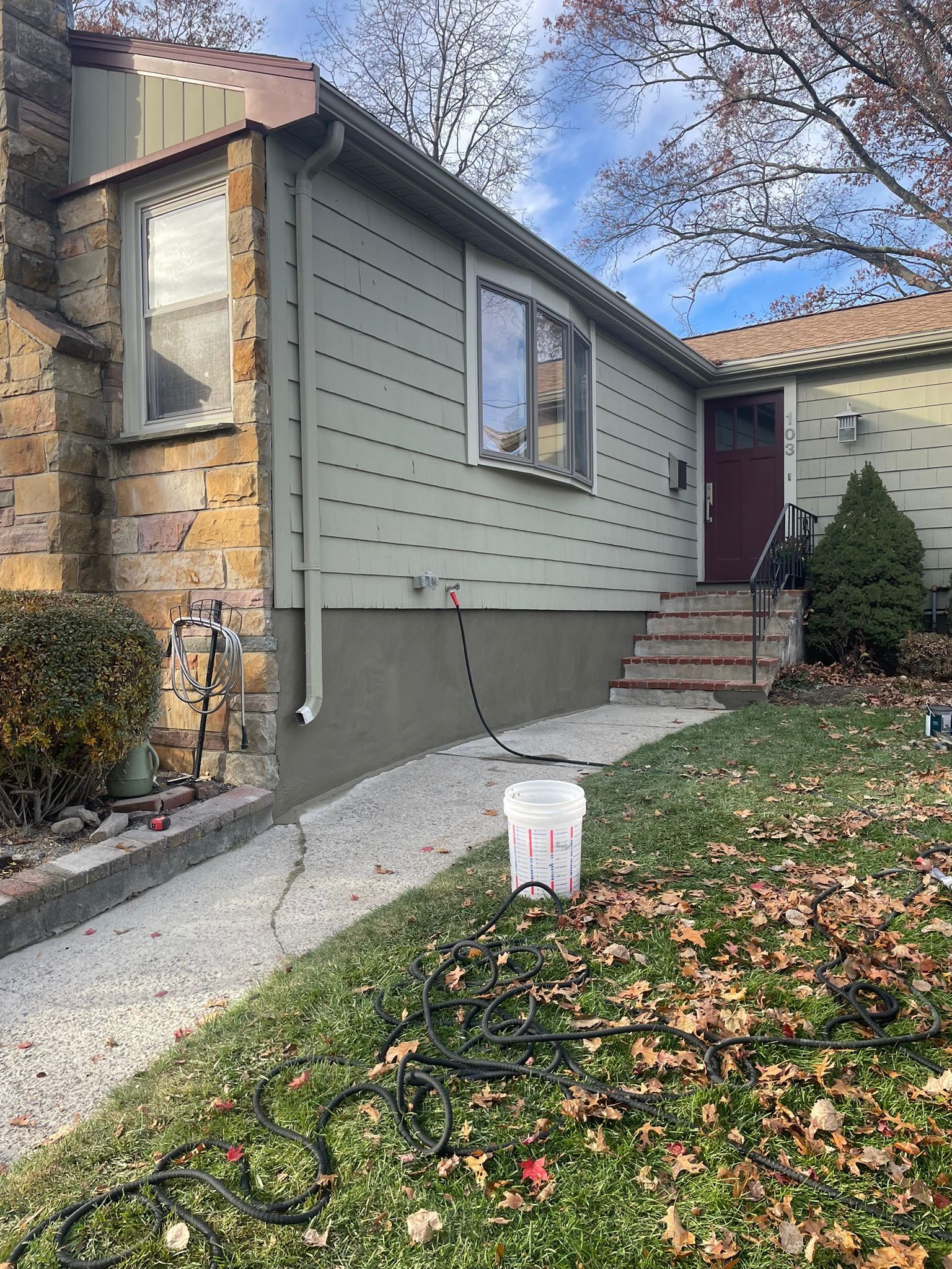 House exterior with stone and siding, walkway, and steps leading to a door; grass and fallen leaves in foreground.