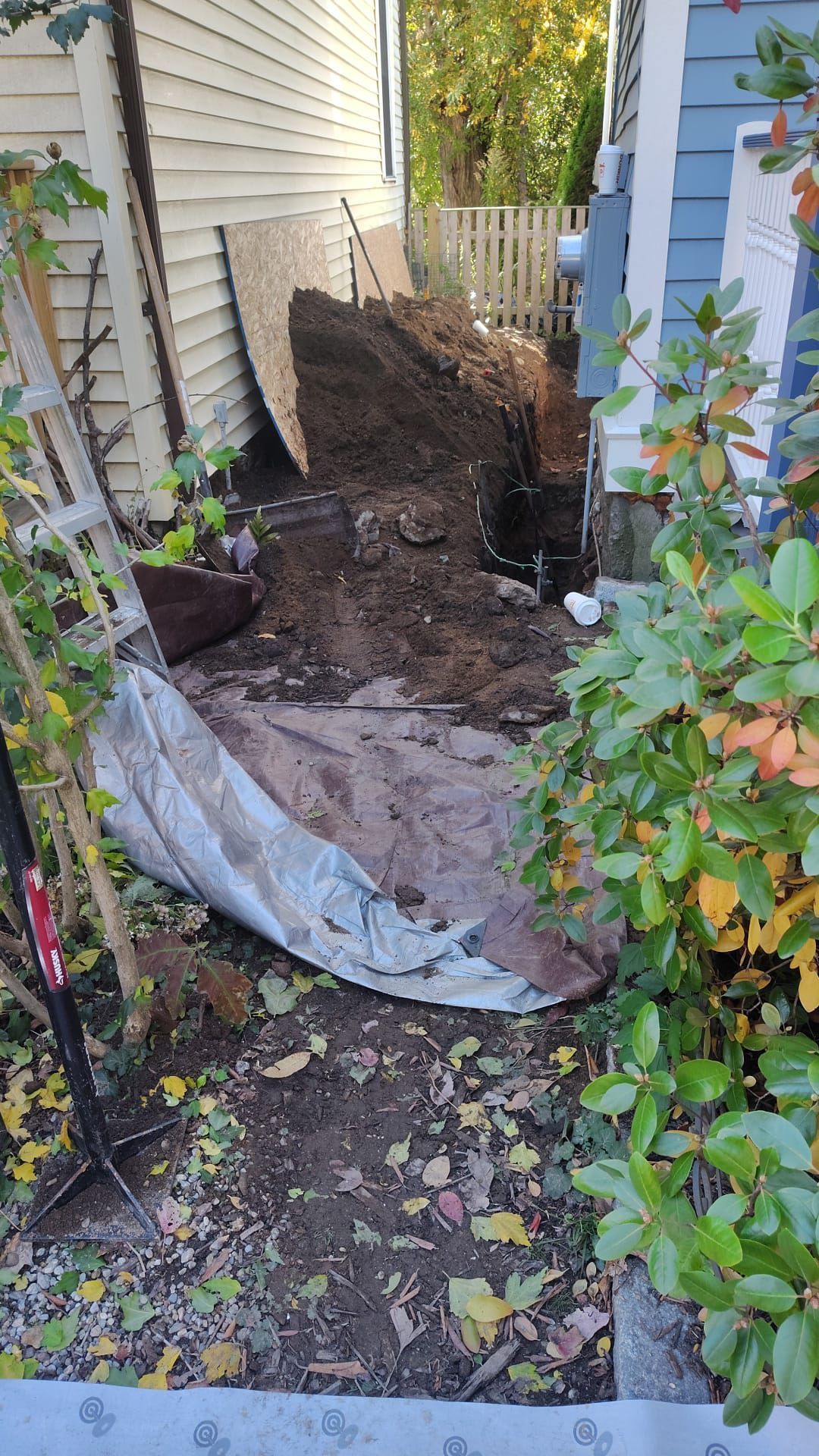 Narrow outdoor space with dirt pile, tarp, tools, and weathered building walls.