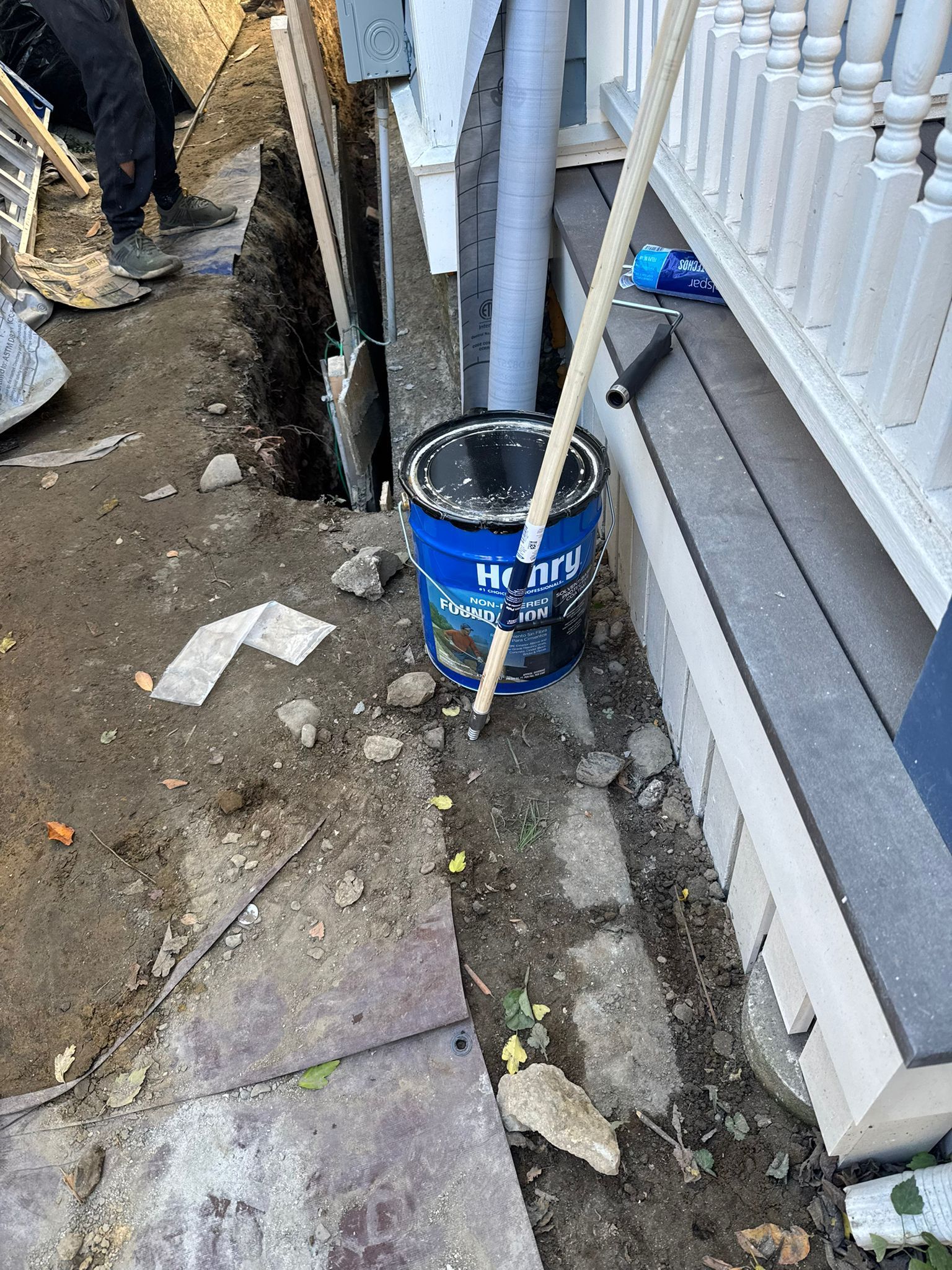 Construction site: a trench dug near a house with tools and a blue paint bucket.