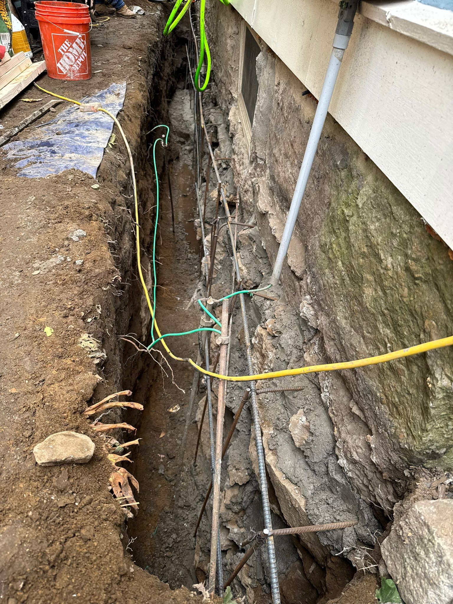 Trench alongside a building foundation with utility lines and pipes visible.