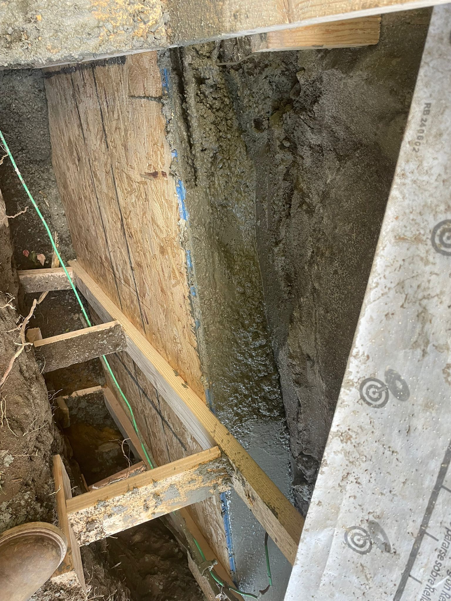 Moldy, unfinished construction interior: wooden beams, particleboard with visible mold, green wire, and damp surface.