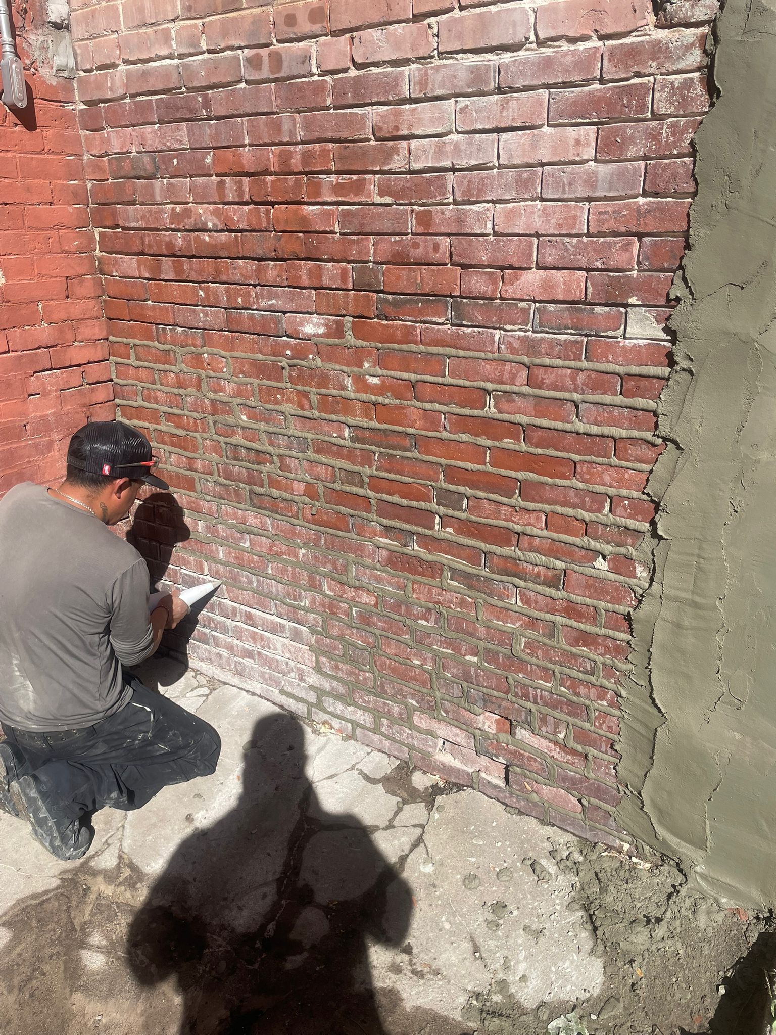Person applying mortar to a brick wall; part of the wall is covered, part uncovered.