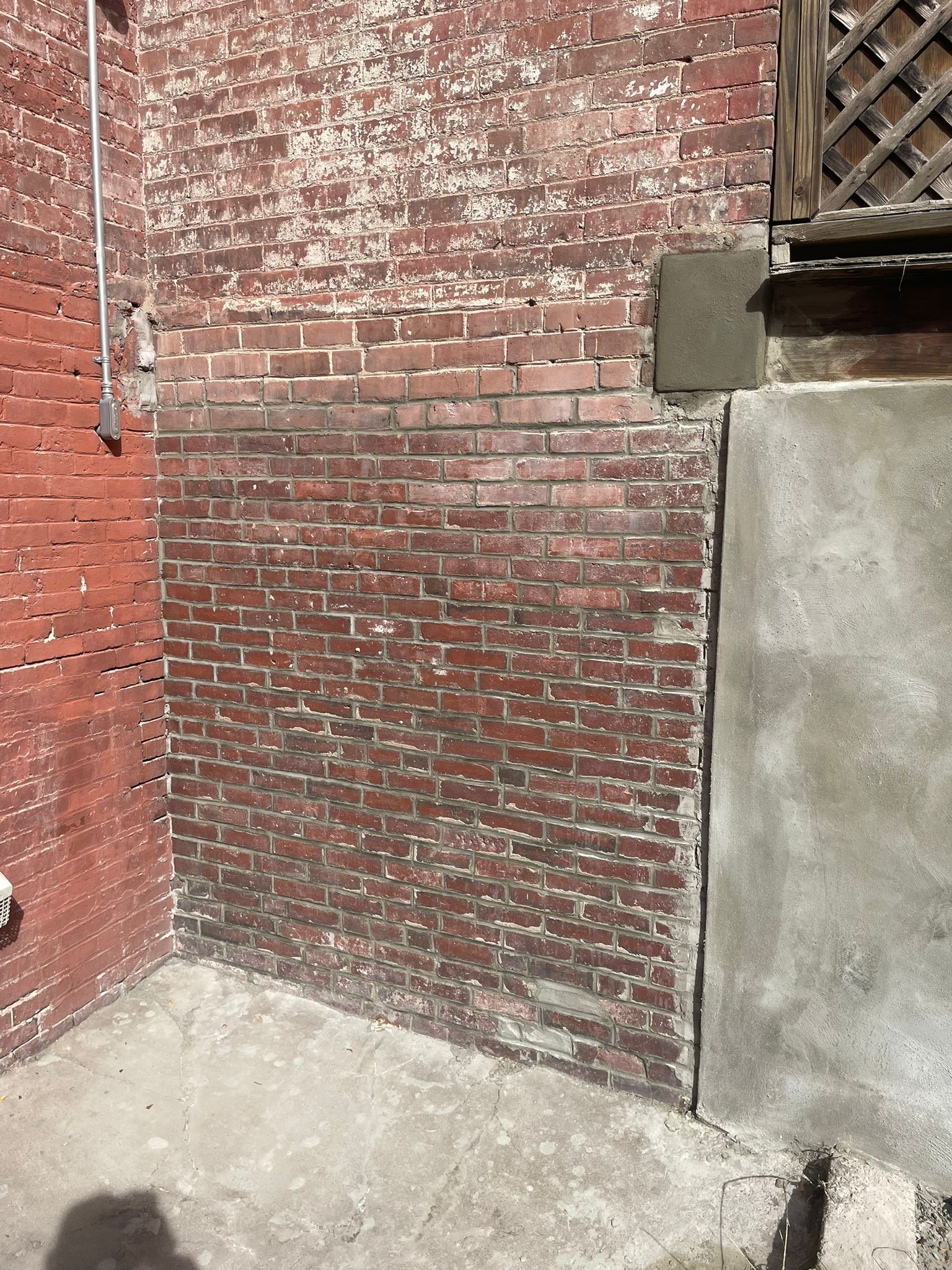 Red brick wall with cement patch and base. Concrete ground.