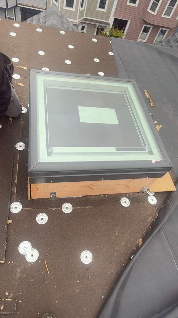 Skylight installed on a dark roof with white fasteners. A person kneels nearby.