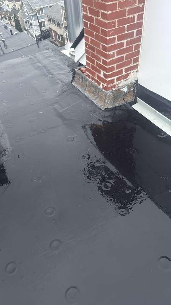 Black, wet flat roof with a brick chimney and rain puddles.