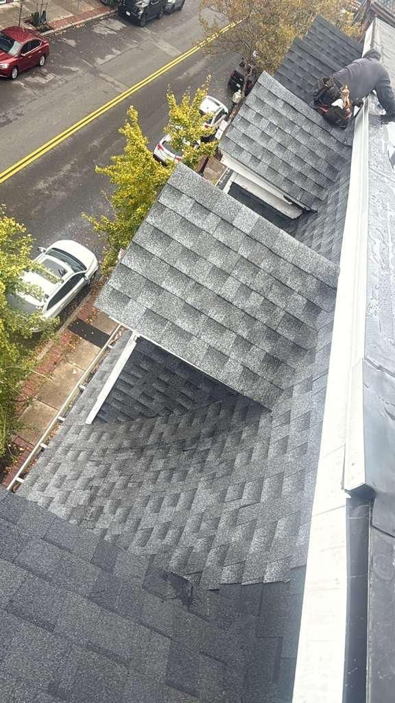 Roofer working on a gray shingle roof. Street and cars below; overcast day.