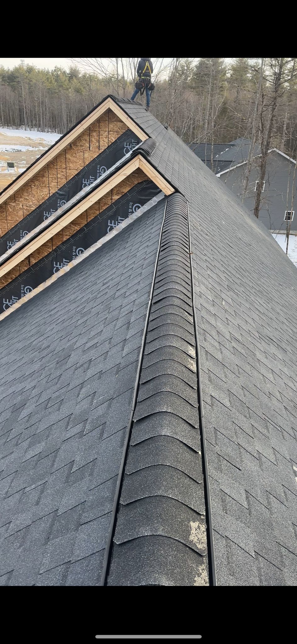 Close-up view of a shingled roof with a ridge, a chimney, and a small area of visible snow.