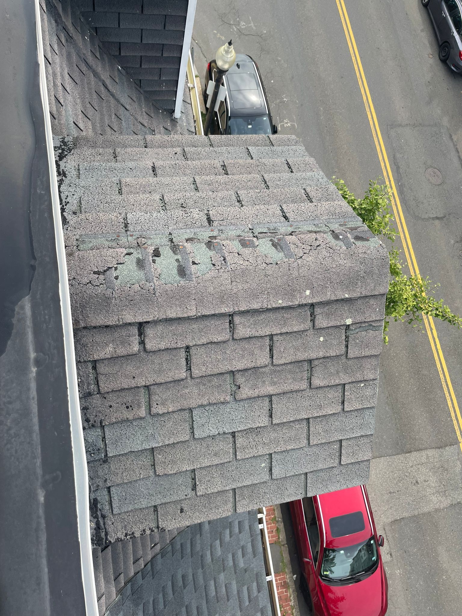 View from above of shingled chimney on rooftop, adjacent to a street and parked cars.