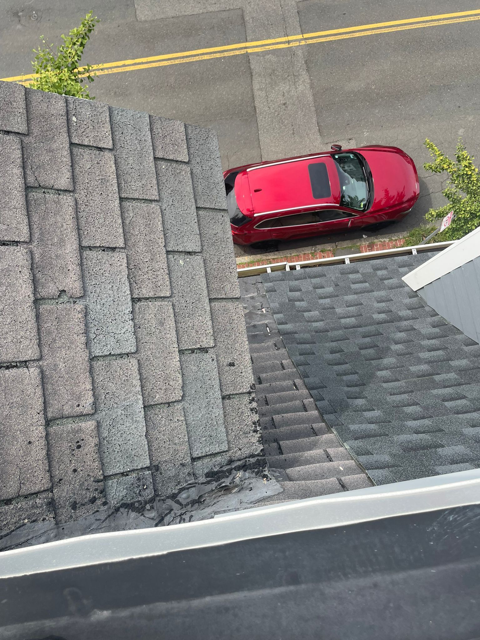 Red car parked near a building with a gray shingled roof, on a street with yellow lines.