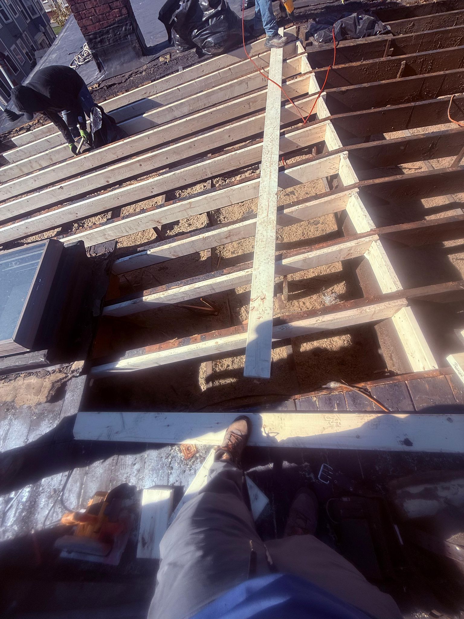 Rooftop construction: Person standing, building roof frame, with boards, tools, and another worker nearby.