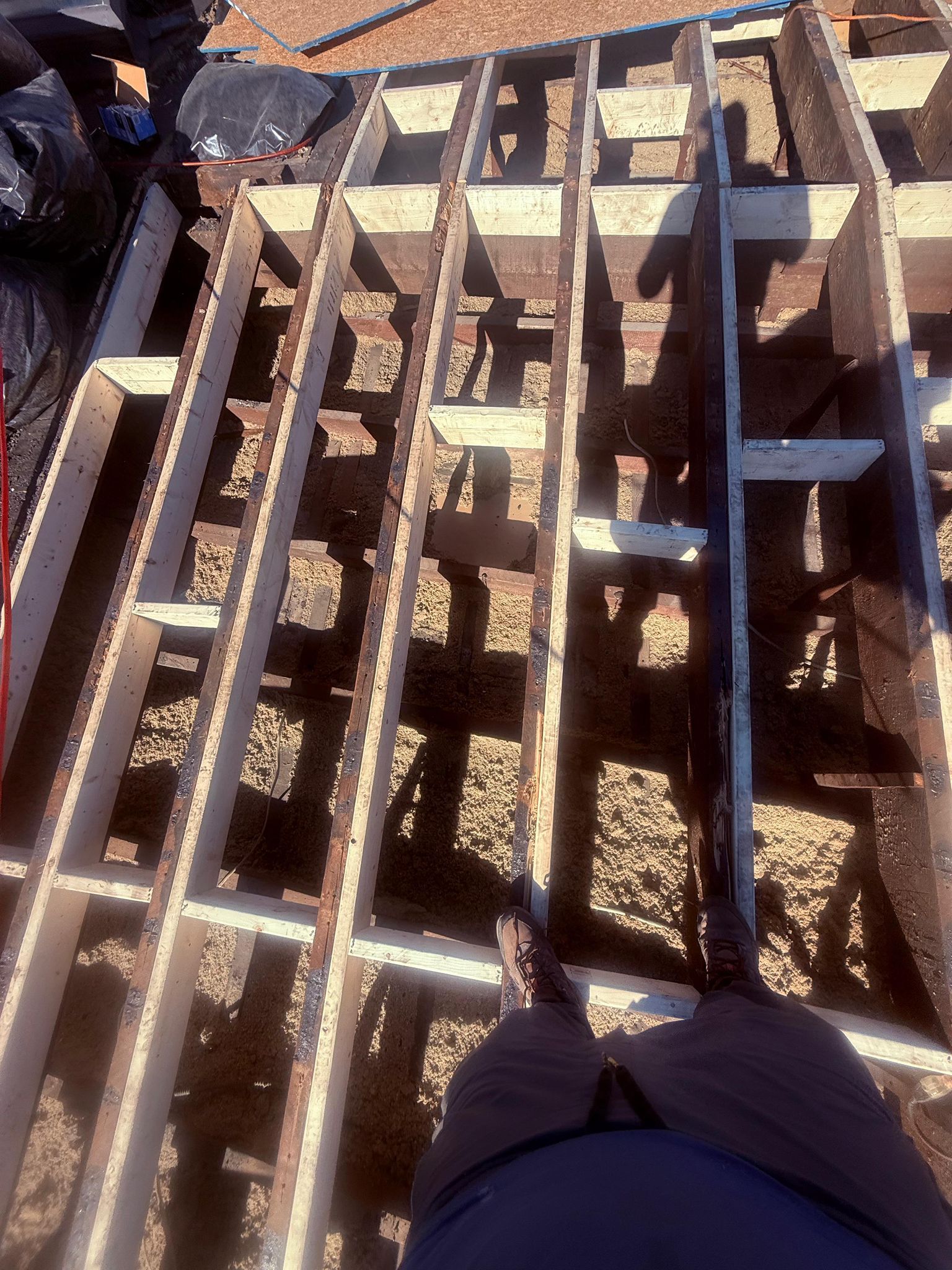 Overhead view of a partially dismantled wood structure on a sunny day; person's legs and feet visible.