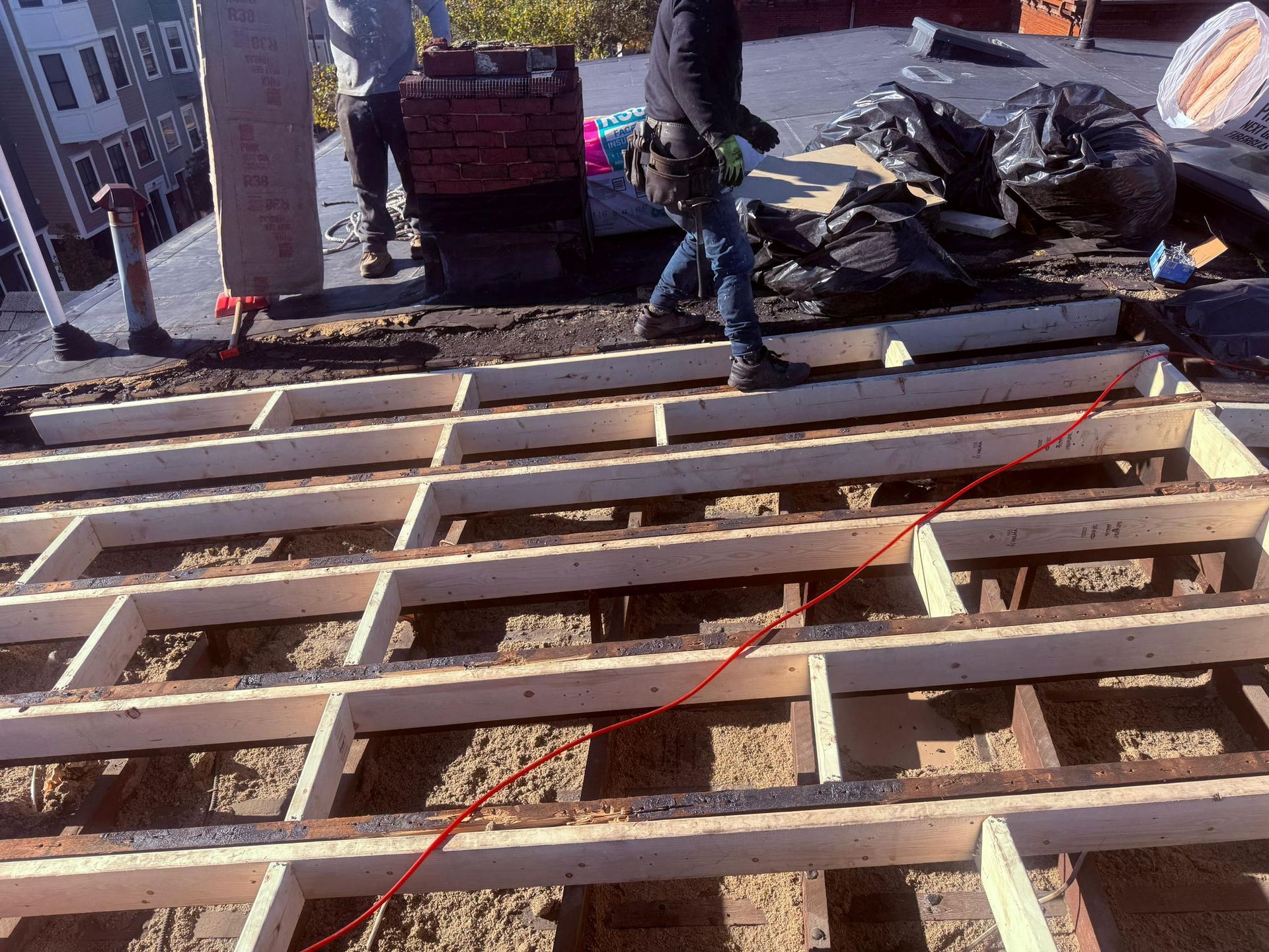 Workers on a roof with wooden beams laid, preparing for construction. One is walking, red line drawn.