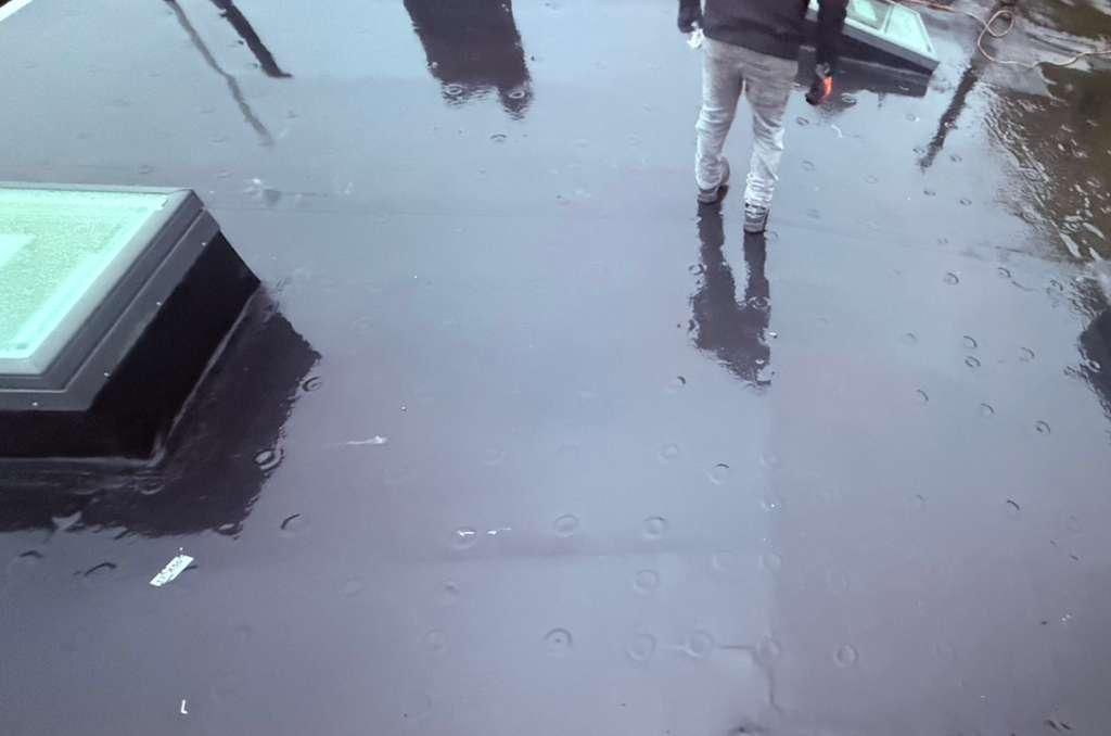 Person walking on a wet, reflective rooftop, reflections of sky and objects visible.